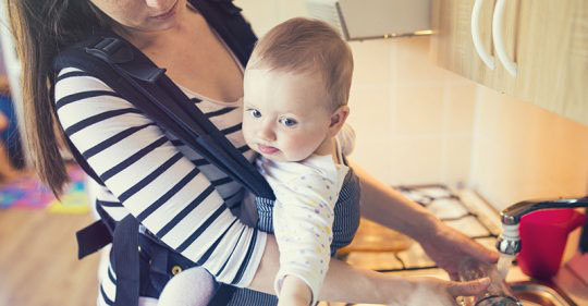 Mother carrying her baby in a baby carrier while dishwashing