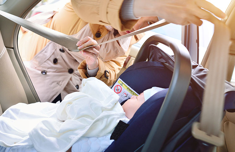 Mother adjusting the safety straps in the baby car seat.